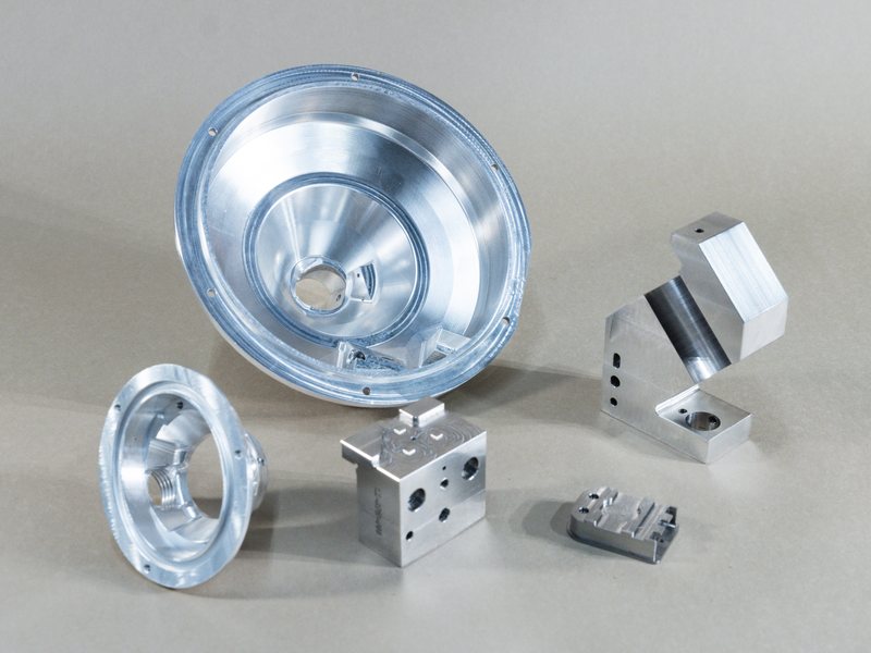 Five milled parts: two round housings, a ported block, an angled bracket, and a small pocketed plate